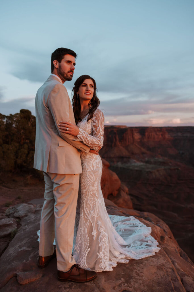 couple embraces on overlook at Arches National Park sunset elopement