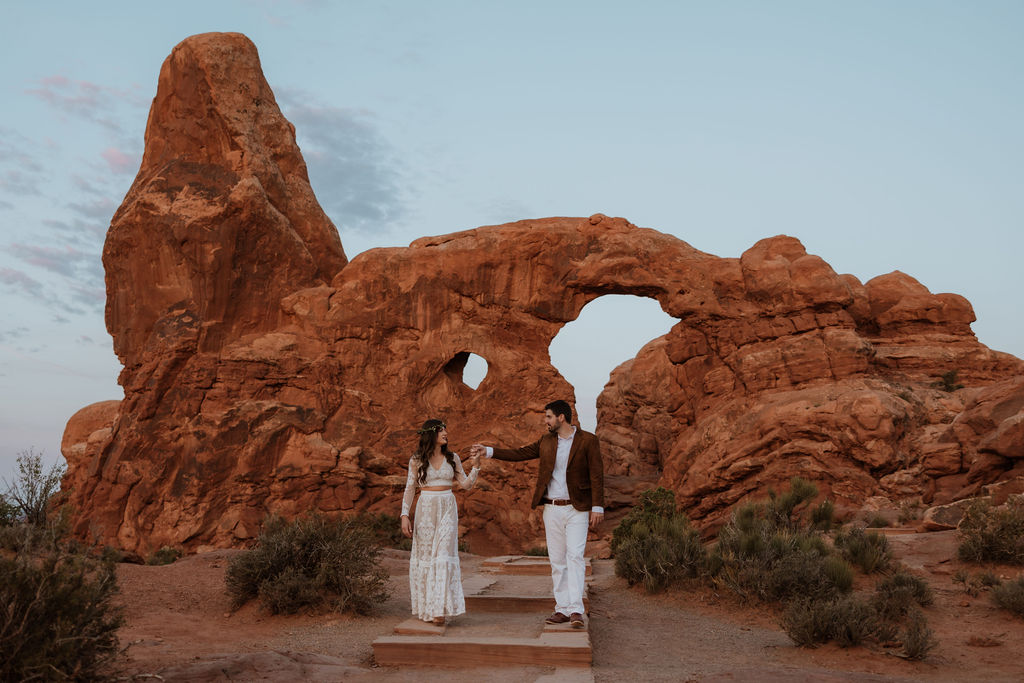 couple holds hands walking around Arches National Park