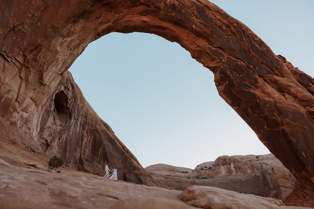 couple walks under Corona Arch on BLM land in Moab Utah 
