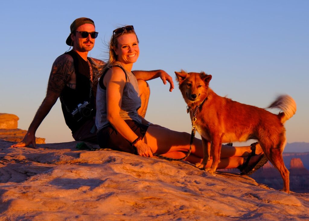couple poses with dog on rock at sunset