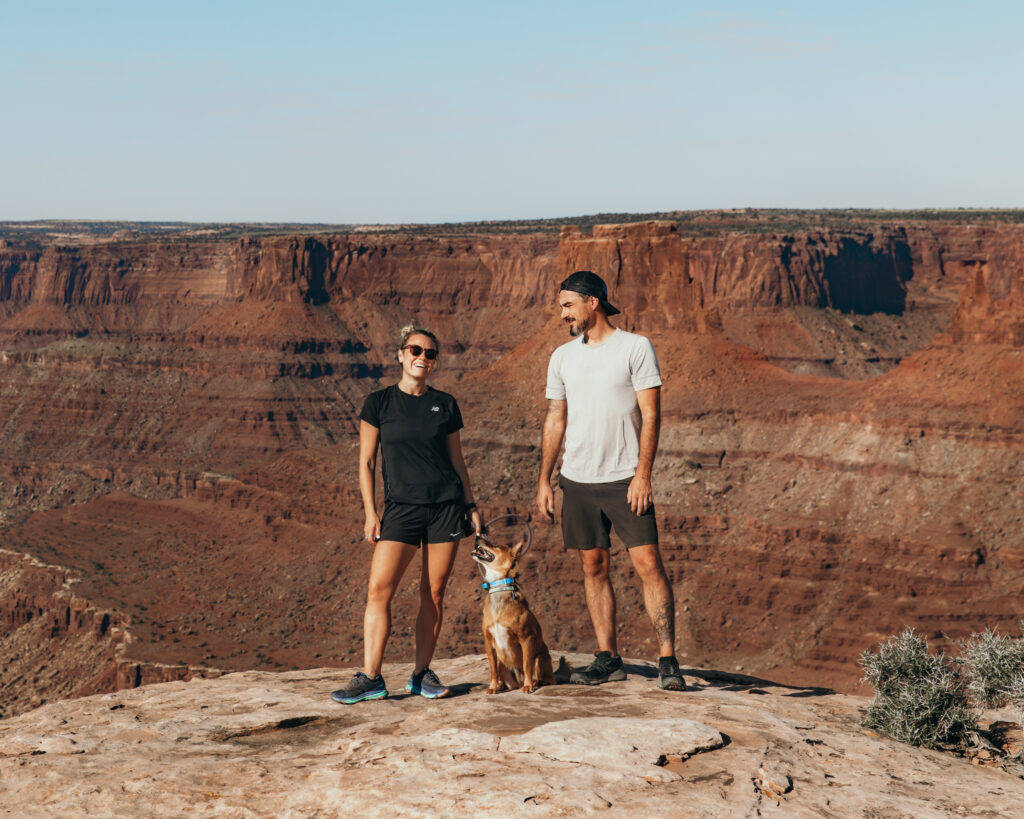 couple poses with dog on rock in Moab