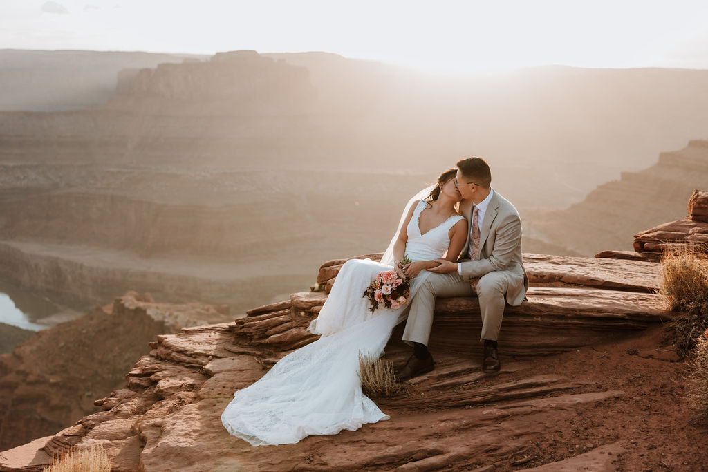 couple sits together on cliff edge at Moab sunset elopement