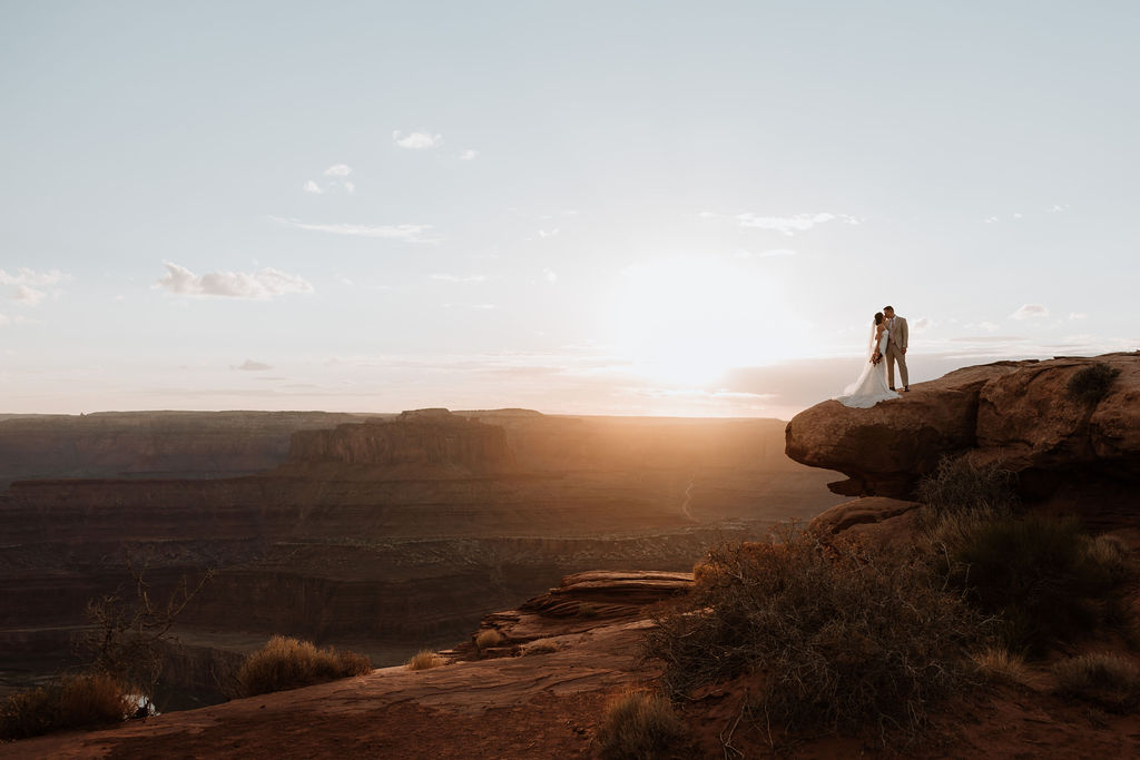 couple poses together at edge of cliff at Moab sunset elopement