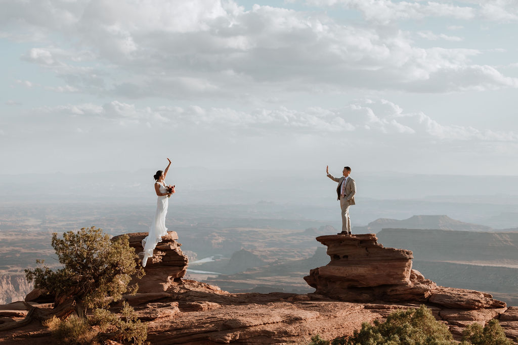 couple waves at each other on cliff edge at Dead Horse Point elopement