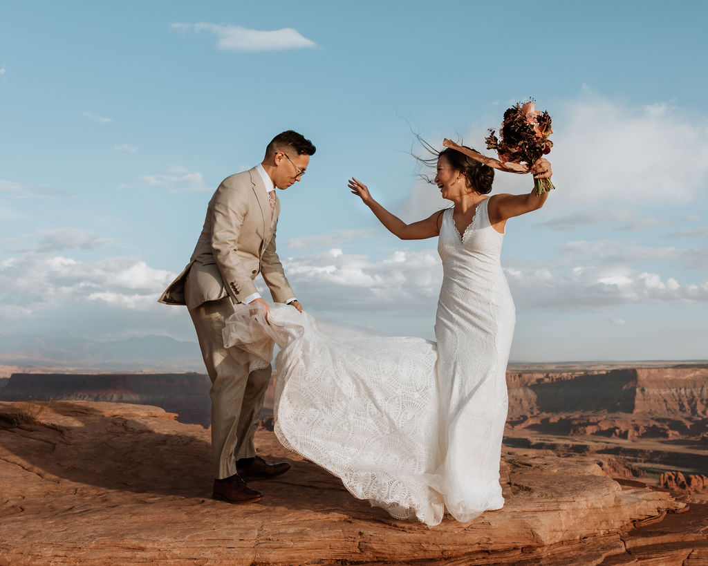 couple catches wedding dress train in wind at Moab elopement