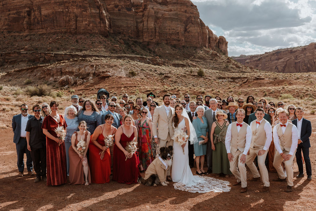 couple poses with dog and wedding guests at Moab desert wedding