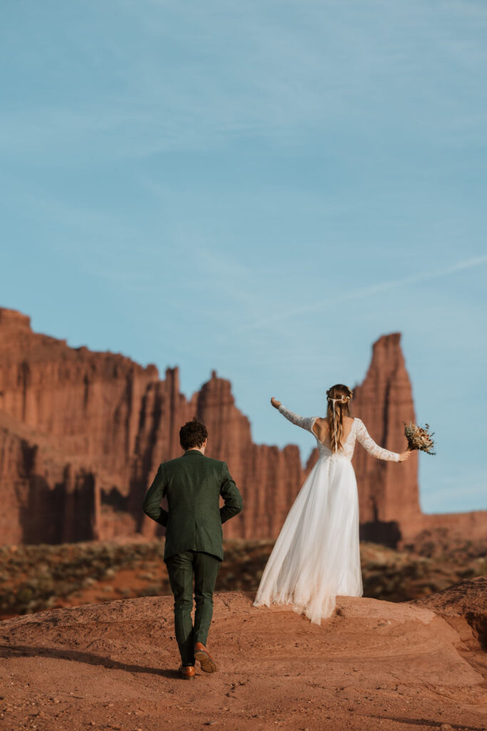 Couple walks up to the top of a cliff during their Castle Valley Utah Elopement