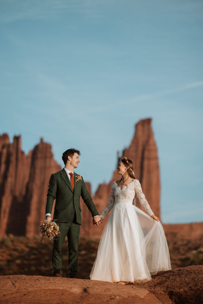 Couple holds hands at the top of a cliff during their Castle Valley Utah Elopement