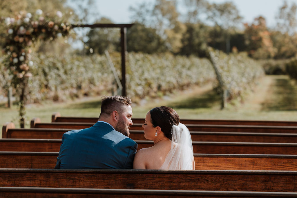 couple sits in wooden wedding pews