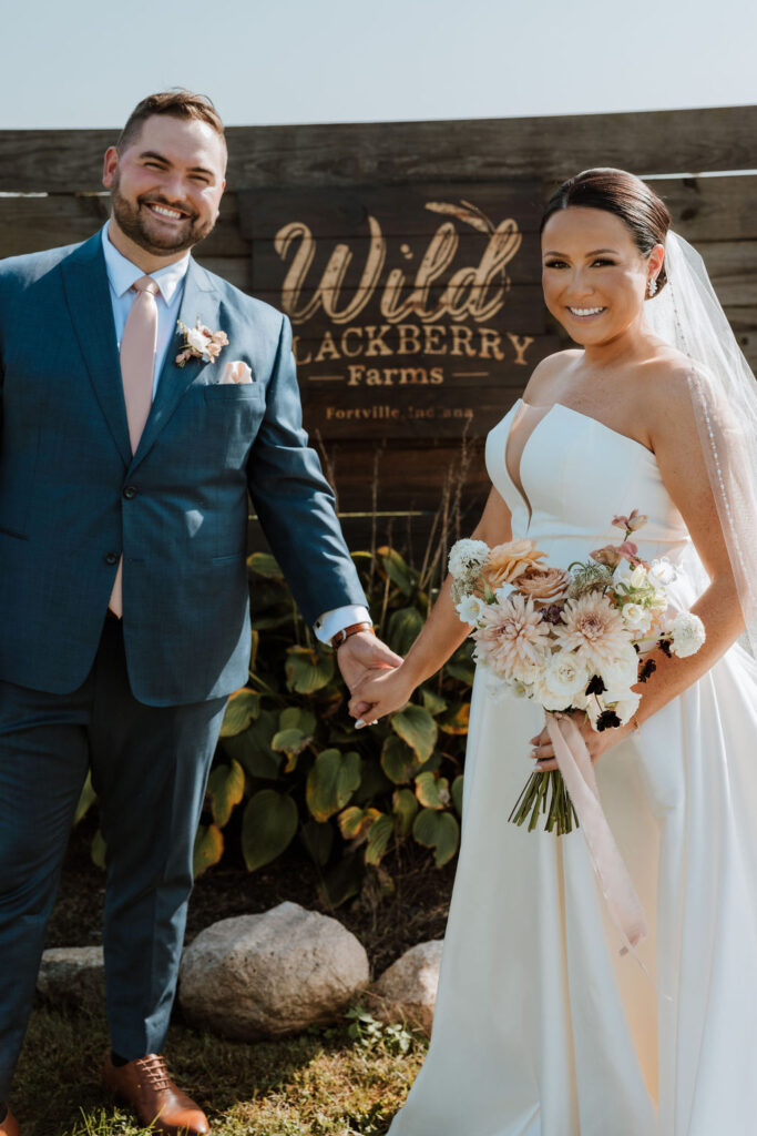 couple poses in front of sign at farm wedding venue