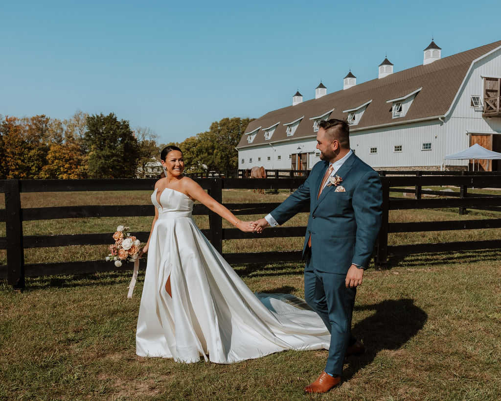 couple walks holding hands at farm wedding