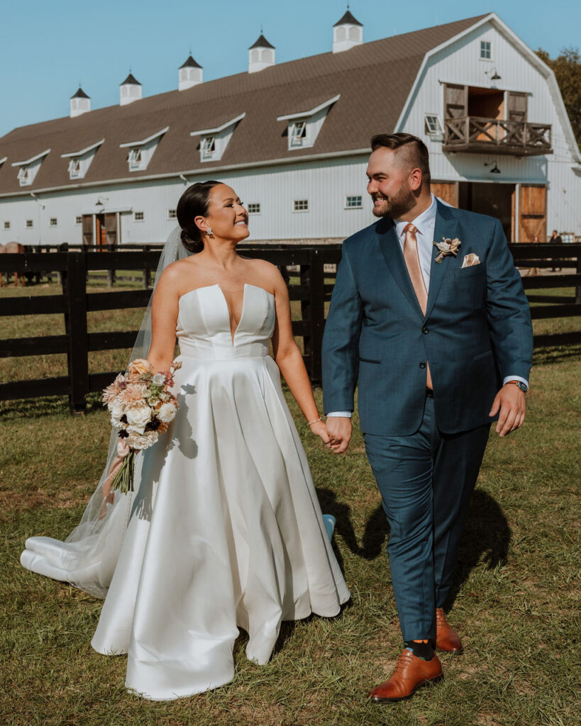 couple walks holding hands at outdoor wedding venue