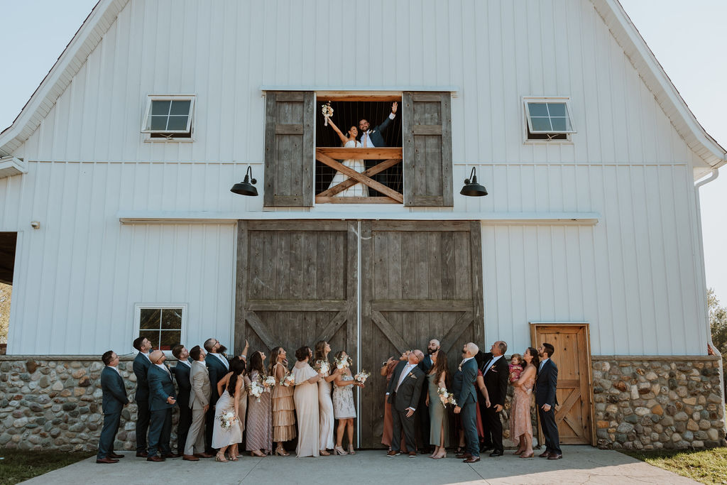 couple stands in barn with wedding party at barn wedding