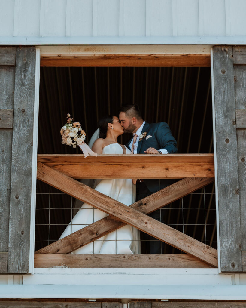 couple kisses in barn wedding venue