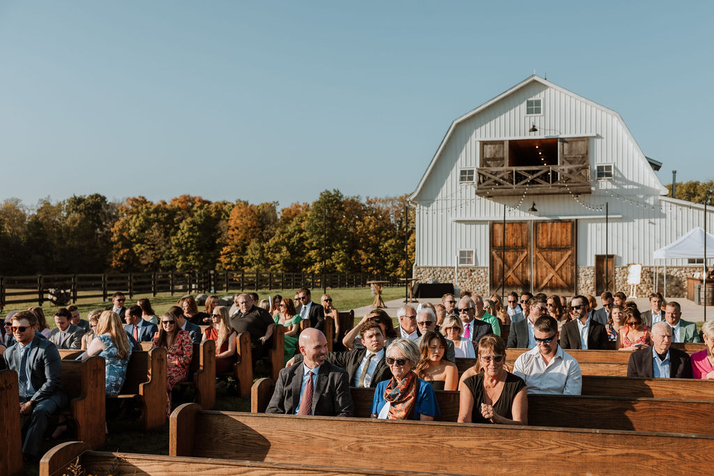 guests sit in wooden pews at barn outdoor wedding
