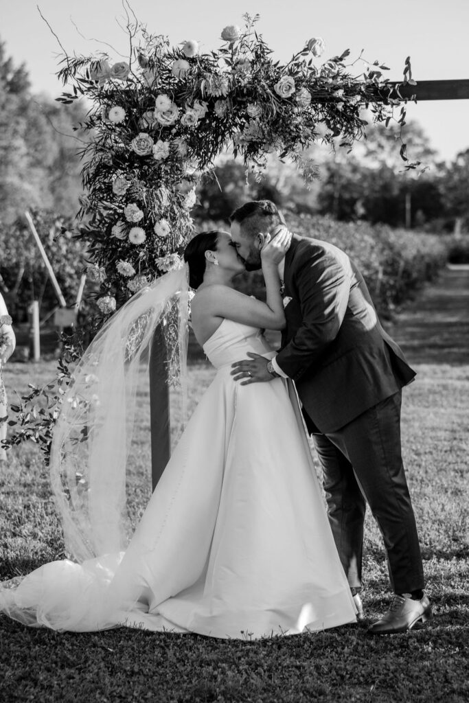 couple kisses under floral wedding arch