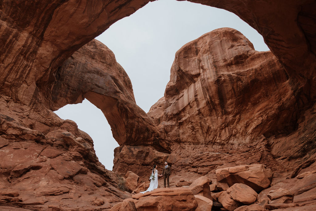couple stands under arch at Arches National Park