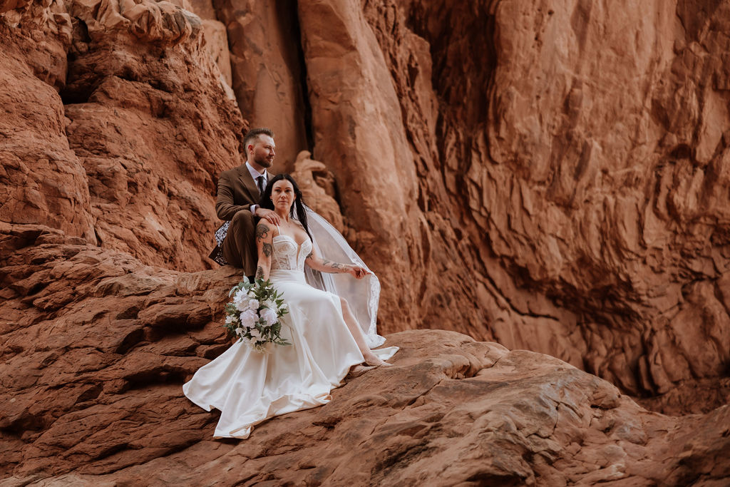 couple sits on red rock at Moab elopement