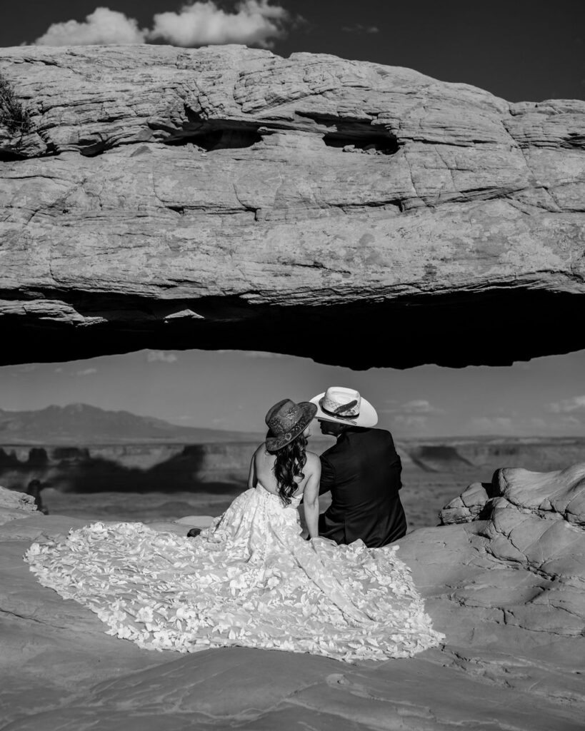 couple sits under arch at canyonlands national park