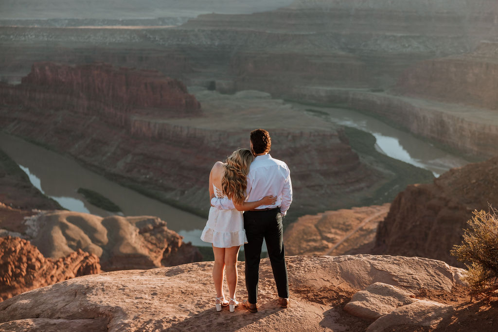 couple standing on rocky ledge overlooking Dead Horse Point