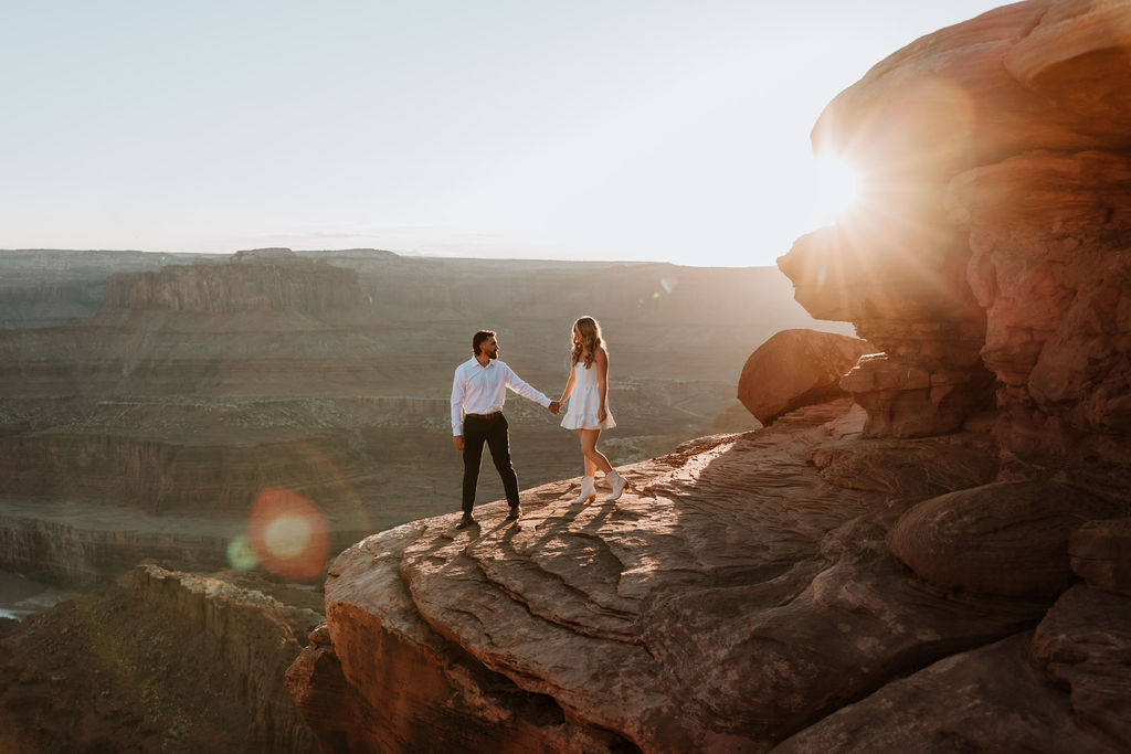 couple holding hands on rocky ledge at Dead Horse Point