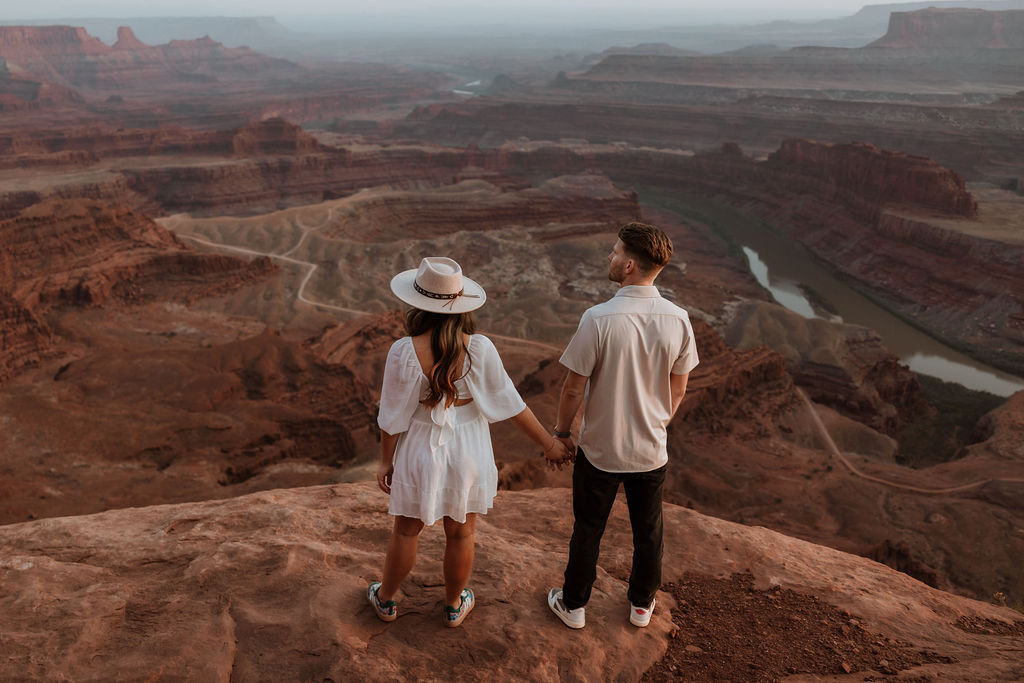 couple standing on rocky ledge overlooking Dead Horse Point
