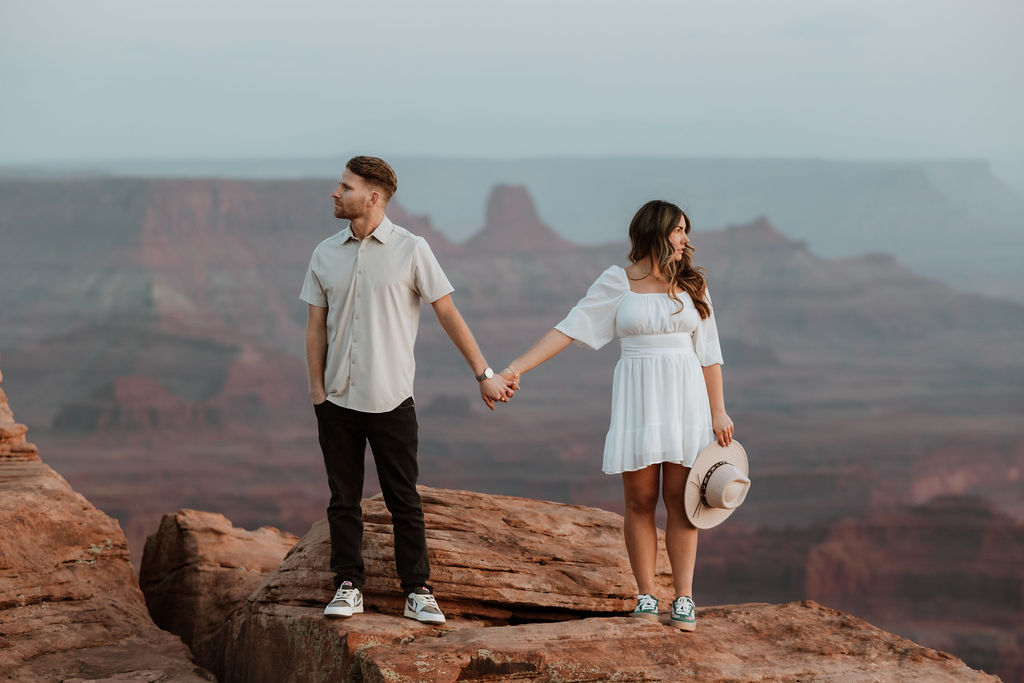 couple holding hands on rocky ledge at Dead Horse Point