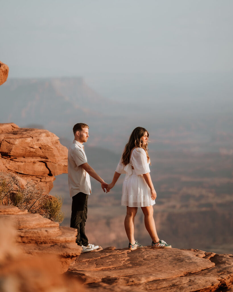 couple holding hands on rocky ledge at Dead Horse Point