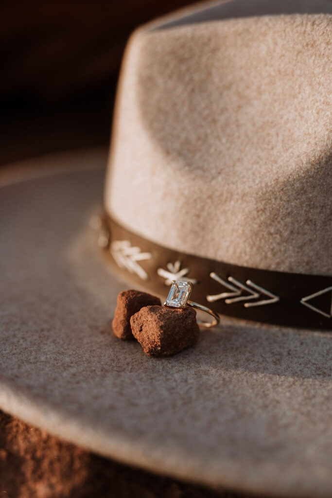 engagement ring sits on red rock beside hat