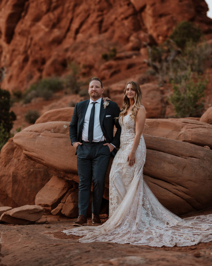 couples stands beside red rock at Arches National Park