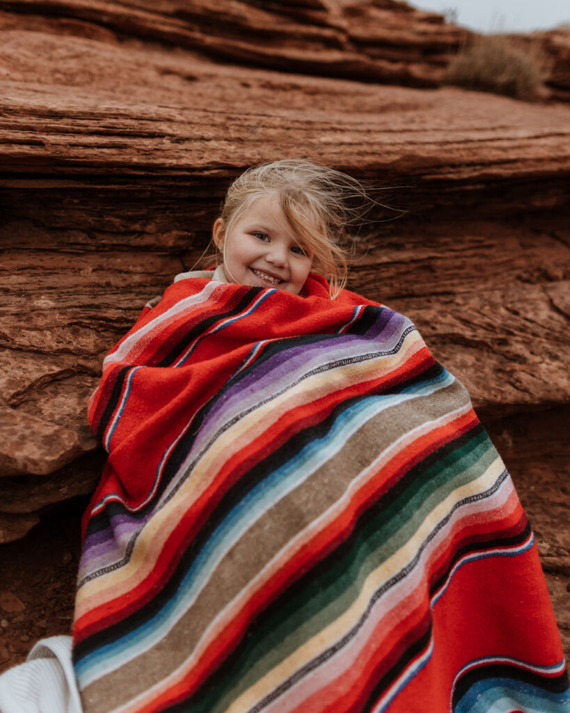 little girl snuggled with blanket against rocks 