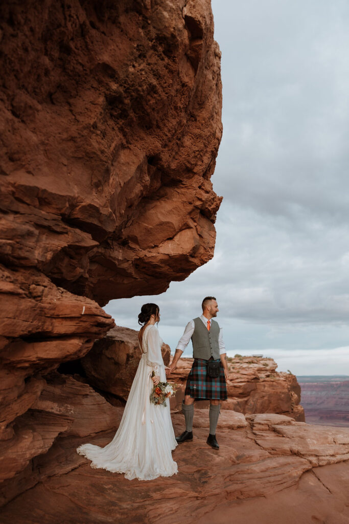couple standing on ledge overlooking Moab's red rock landscape