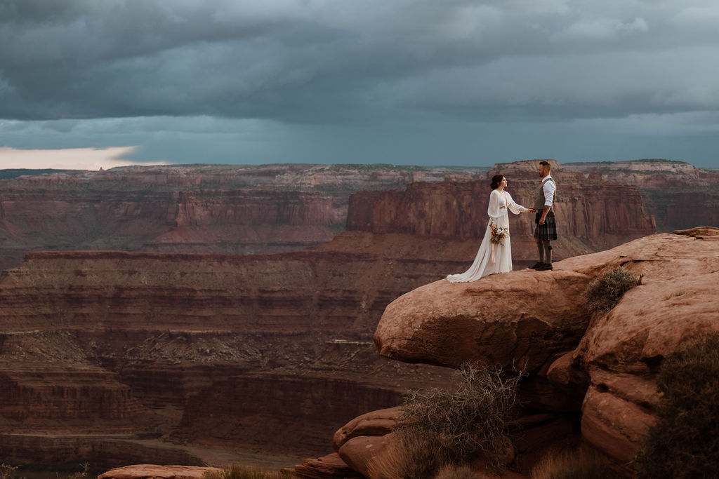couple standing on ledge overlooking Moab's red rock landscape