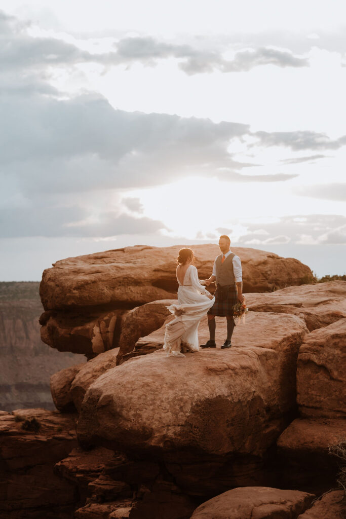 couple standing along ledge overlooking Moab's red rock landscape