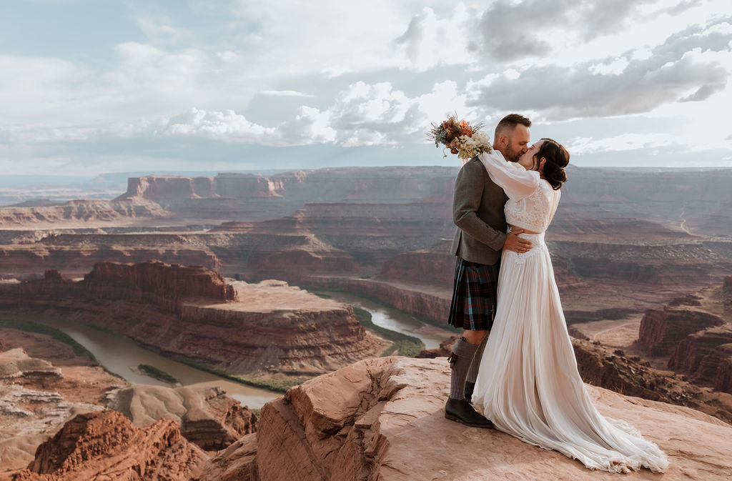 couple kissing on ledge overlooking Moab's red rock landscape