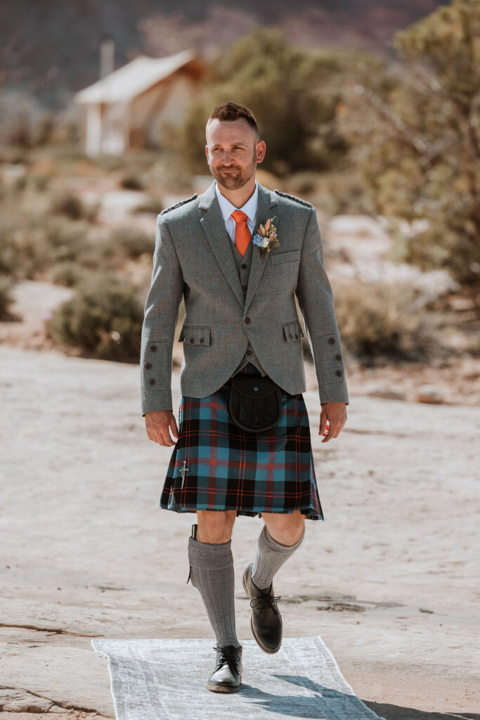 groom walking down aisle wearing kilt for under canvas moab wedding