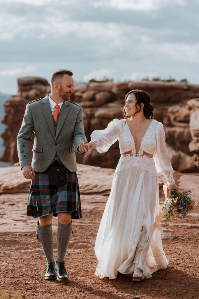 couple holding hands walking along red rocky path