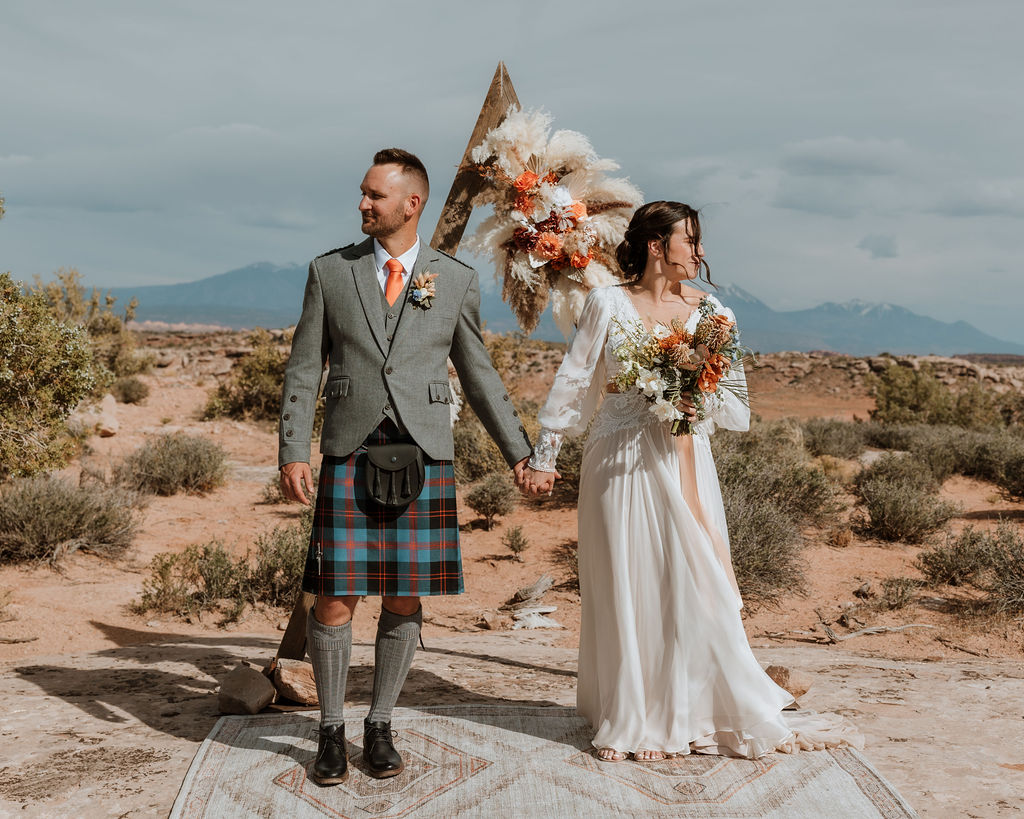 couple holds hands under boho chic wedding arch