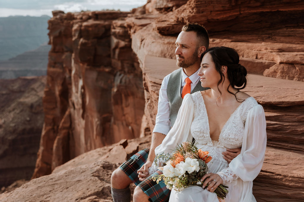 couple sitting on ledge overlooking Moab's red rock landscape