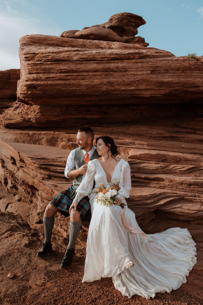 couple sitting on ledge overlooking Moab's red rock landscape
