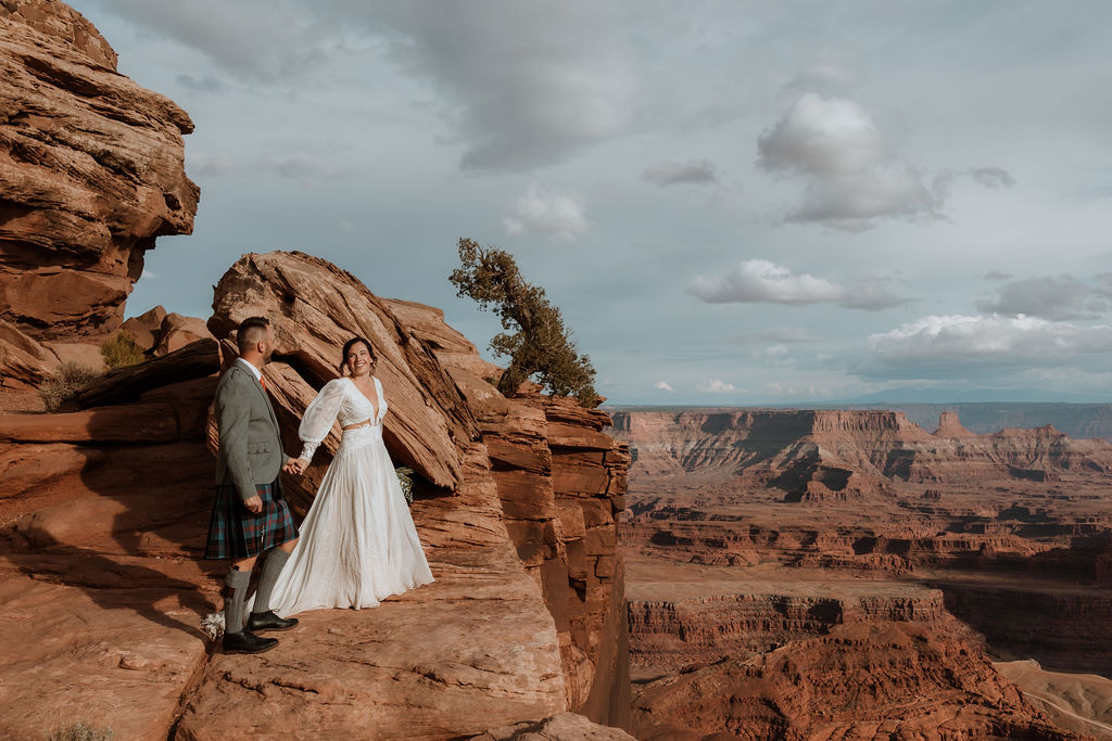 couple holding hands on rocky ledge of moab