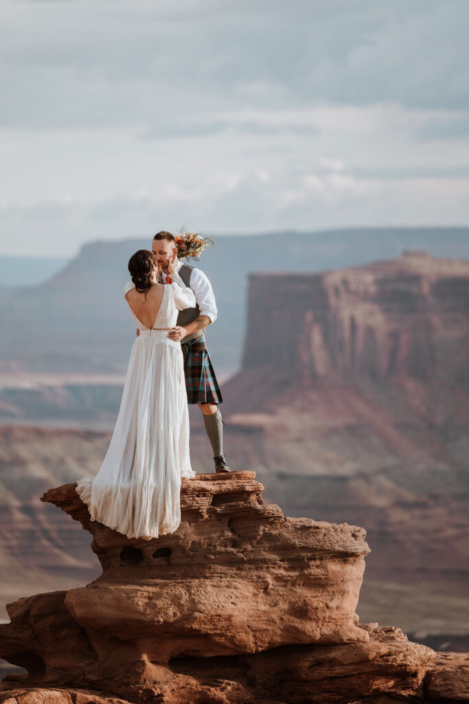 couple kissing on ledge overlooking Moab's red rock landscape