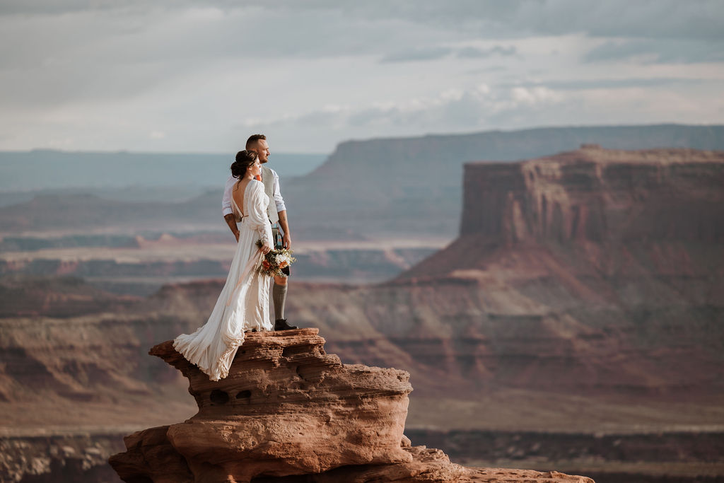 couple standing along ledge overlooking Moab's red rock landscape