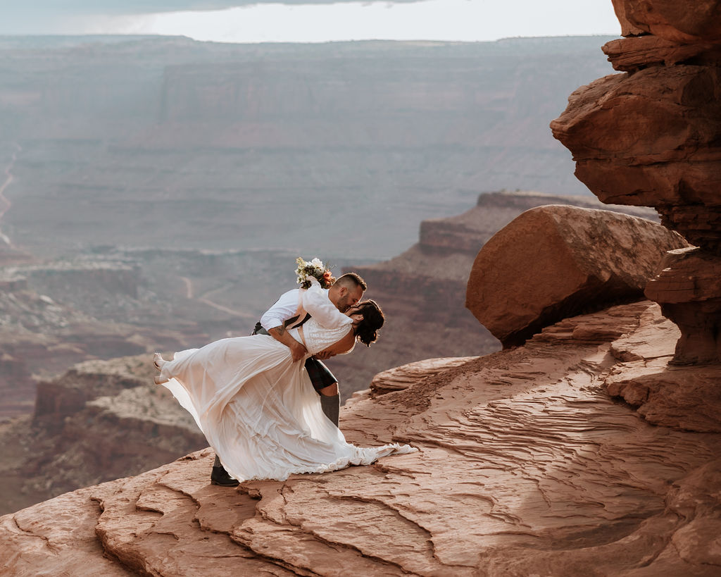 couple kissing along ledge overlooking Moab's red rock landscape