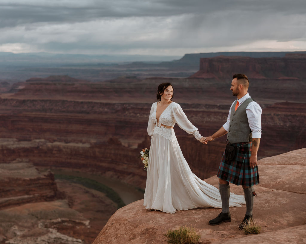 couple standing on ledge overlooking Moab's red rock landscape