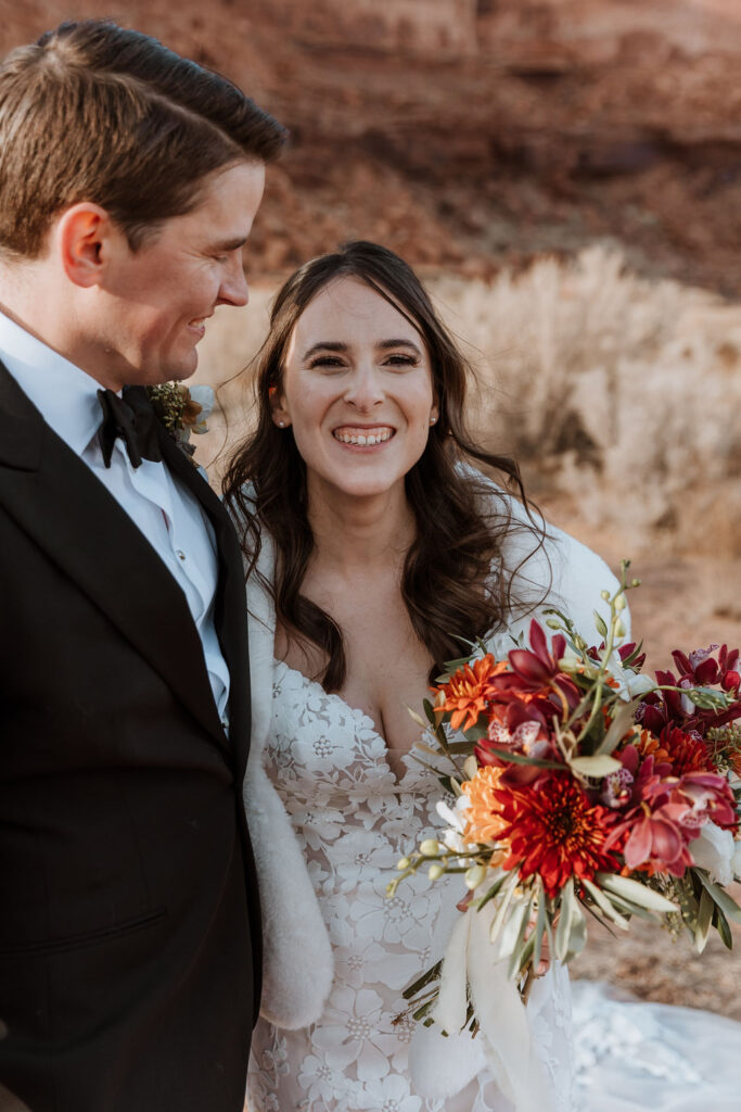 Bride and groom smiling with a vibrant bouquet in Moab