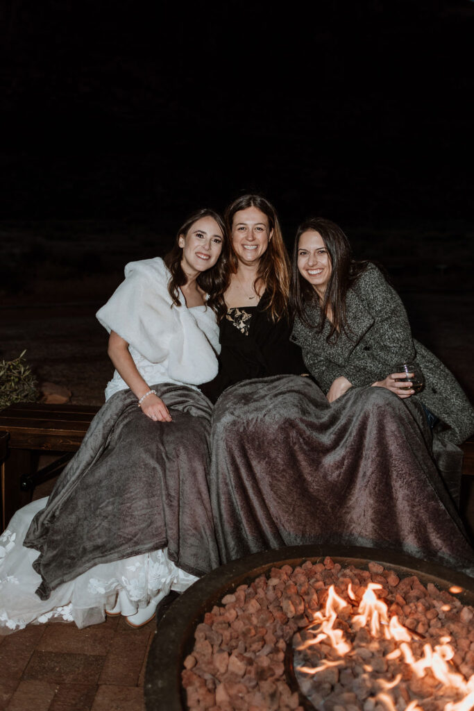 girls huddled together with a blanket around a fire pit 