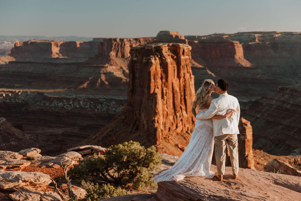 couple kiss along ledge overlooking Moab's rocky landscape