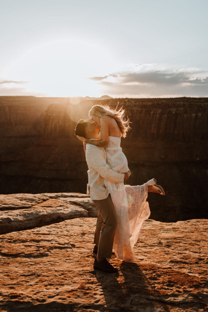 couple kiss along rocky edge during sunset in Moab