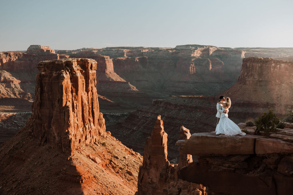 couple kiss along ledge overlooking Moab's rocky landscape